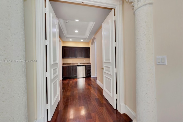 corridor with dark hardwood / wood-style flooring, sink, ornate columns, a raised ceiling, and ornamental molding