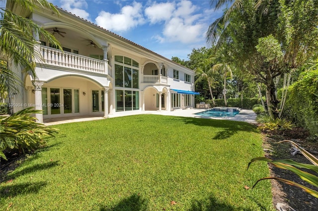 rear view of property featuring a balcony, a patio area, a lawn, and ceiling fan