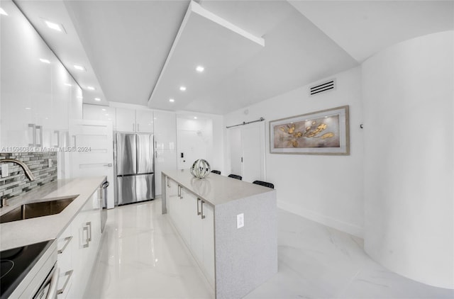 kitchen featuring decorative backsplash, stainless steel fridge, sink, a center island, and white cabinetry