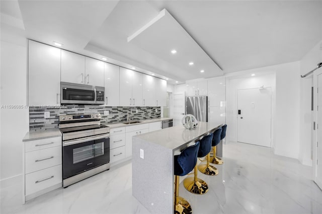 kitchen with white cabinetry, a center island, sink, a breakfast bar, and appliances with stainless steel finishes