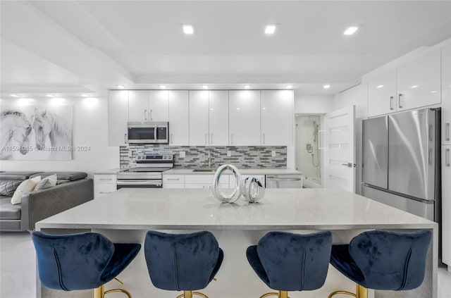 kitchen with white cabinets, appliances with stainless steel finishes, a kitchen bar, and tasteful backsplash