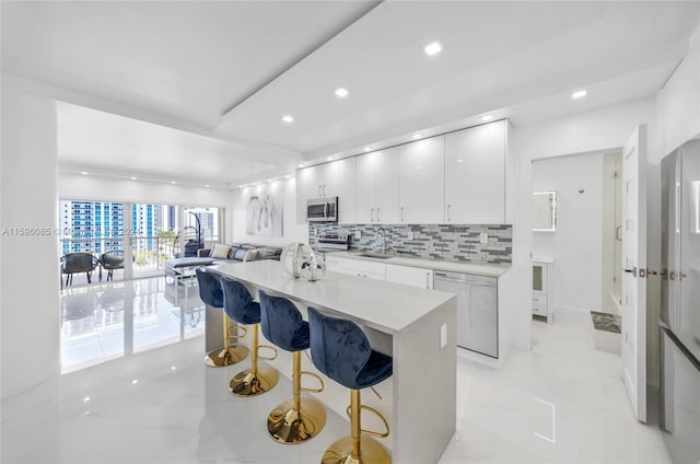 kitchen featuring white cabinetry, sink, decorative backsplash, a breakfast bar, and appliances with stainless steel finishes