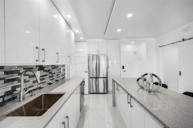 kitchen with white cabinetry, sink, light stone countertops, decorative backsplash, and appliances with stainless steel finishes