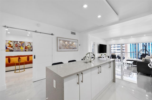 kitchen featuring a barn door, white cabinetry, and light stone counters