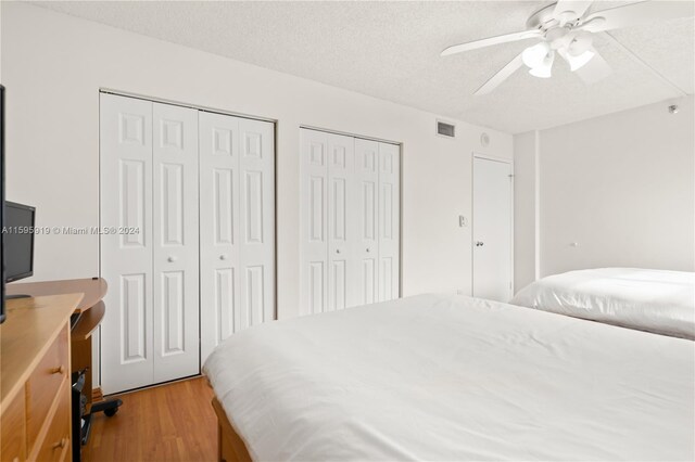 bedroom featuring multiple closets, wood-type flooring, ceiling fan, and a textured ceiling