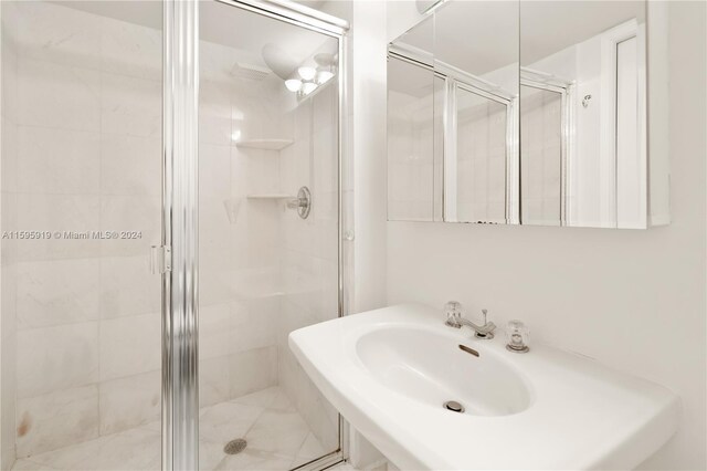 bathroom featuring a shower with shower door and sink