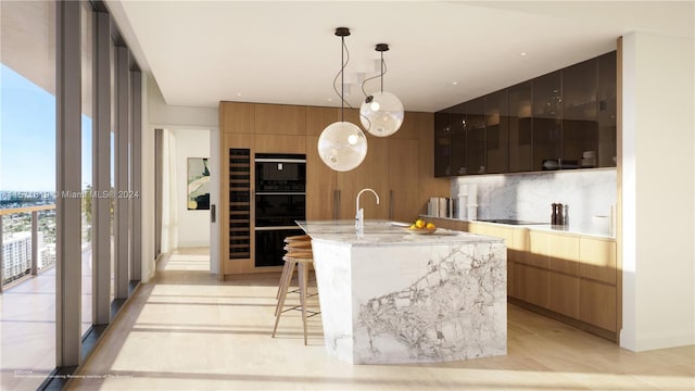 kitchen featuring an island with sink, decorative light fixtures, light stone counters, sink, and a kitchen bar