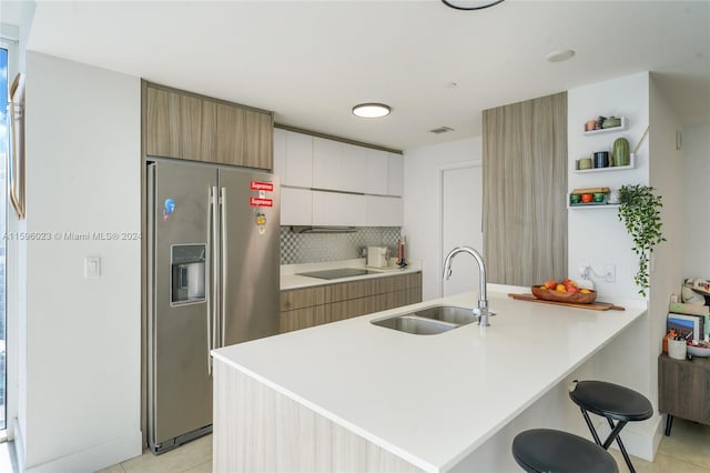 kitchen with white cabinets, sink, stainless steel fridge, light tile patterned flooring, and kitchen peninsula