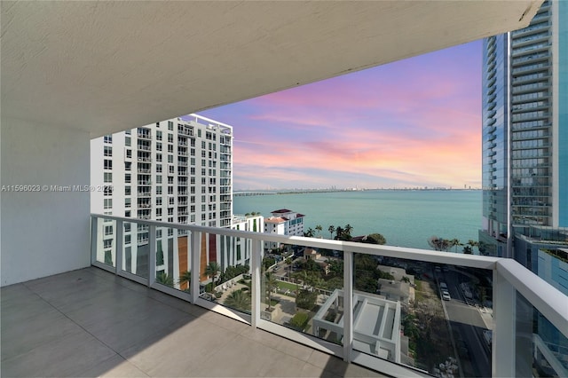 balcony at dusk featuring a water view