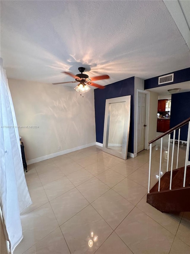 tiled empty room with ceiling fan and a textured ceiling