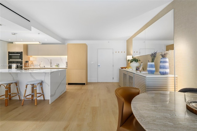 kitchen featuring modern cabinets, a breakfast bar area, decorative light fixtures, multiple ovens, and light wood-type flooring