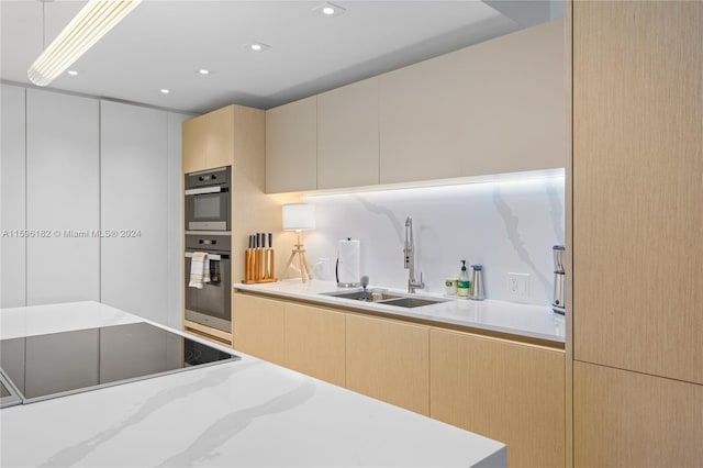 kitchen featuring black electric stovetop, light brown cabinets, a sink, light countertops, and multiple ovens