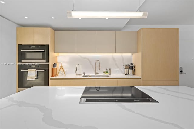 kitchen featuring decorative backsplash, light stone countertops, multiple ovens, stovetop, and a sink