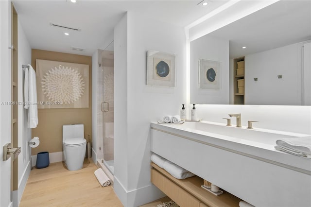 bathroom with toilet, a stall shower, vanity, wood finished floors, and baseboards