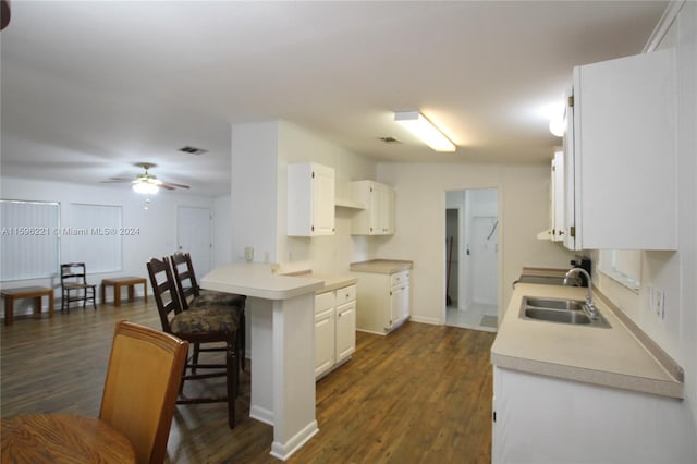 kitchen featuring dark wood-type flooring, sink, a breakfast bar area, white cabinetry, and kitchen peninsula