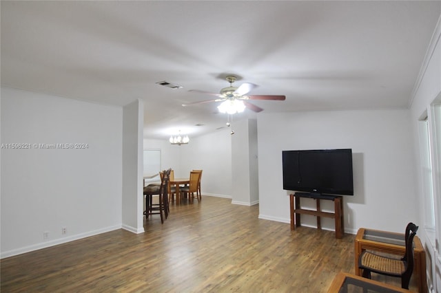 living room featuring crown molding, dark wood-type flooring, and ceiling fan with notable chandelier