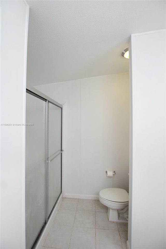 bathroom with a shower with door, tile patterned floors, and toilet