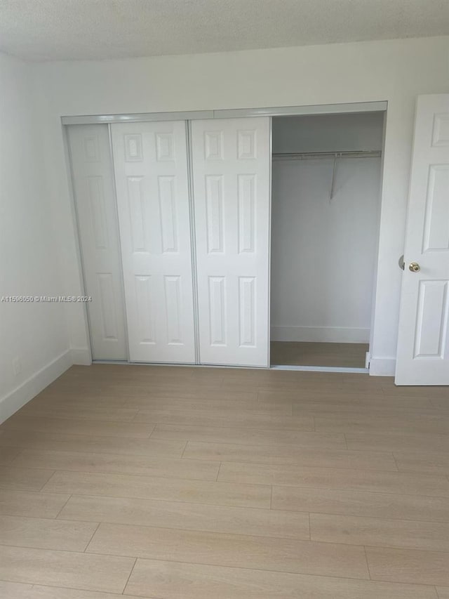 unfurnished bedroom featuring a closet, a textured ceiling, and light wood-type flooring