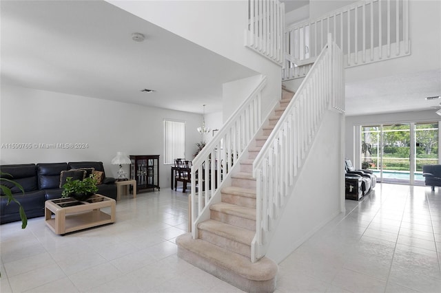 staircase with a towering ceiling, a notable chandelier, and tile patterned floors