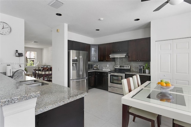 kitchen with sink, appliances with stainless steel finishes, backsplash, dark brown cabinets, and light stone countertops