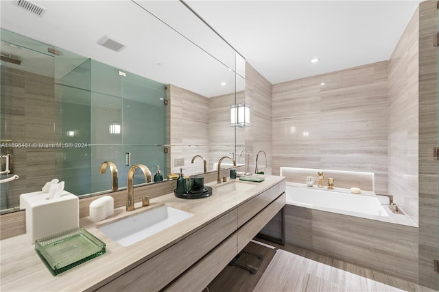 bathroom featuring tile walls, large vanity, plus walk in shower, and dual sinks