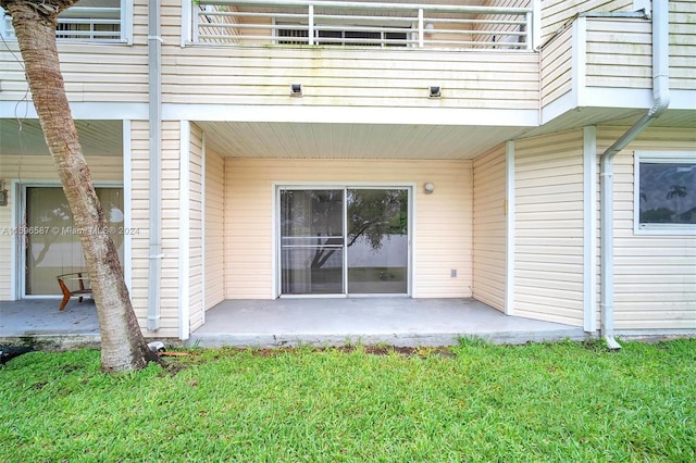 entrance to property featuring a patio area, a balcony, and a yard