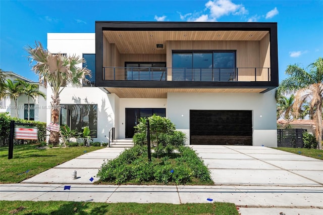 contemporary home featuring a balcony, stucco siding, driveway, an attached garage, and a front yard