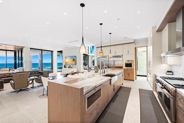 kitchen with hanging light fixtures, wall chimney exhaust hood, built in appliances, a large island with sink, and sink