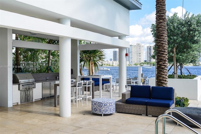 view of patio / terrace featuring exterior kitchen, a grill, an outdoor hangout area, exterior bar, and a water view