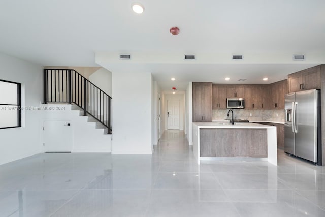 kitchen with an island with sink, stainless steel appliances, light tile patterned floors, and tasteful backsplash