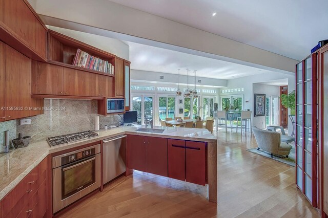 kitchen featuring kitchen peninsula, tasteful backsplash, stainless steel appliances, light wood-type flooring, and pendant lighting