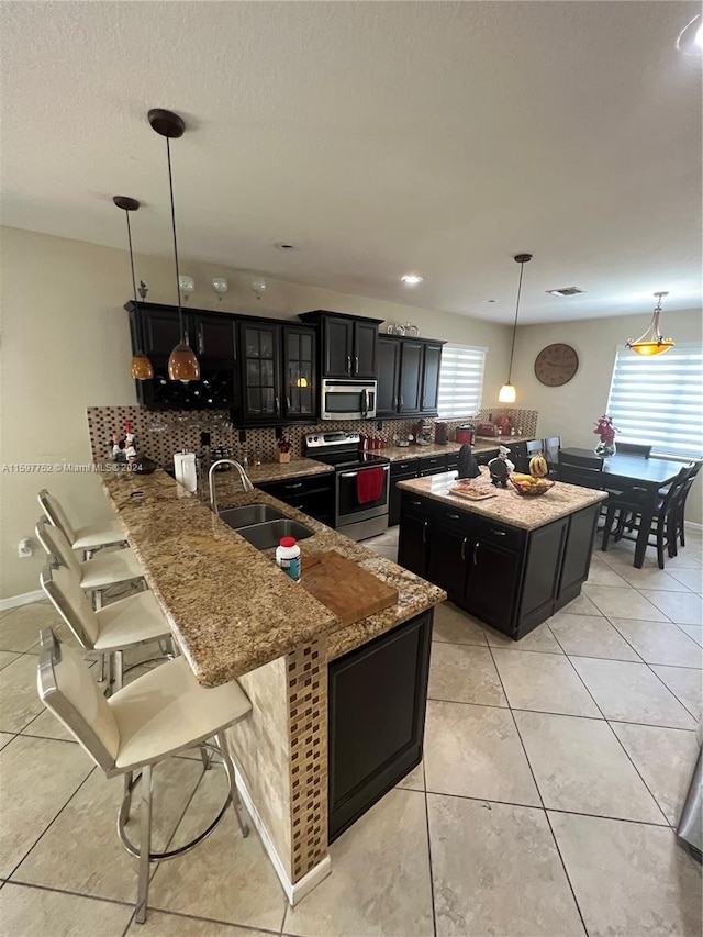 kitchen featuring sink, kitchen peninsula, pendant lighting, decorative backsplash, and appliances with stainless steel finishes