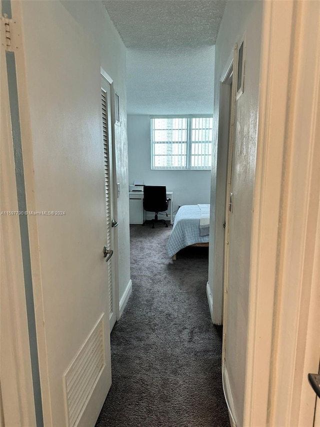 hall featuring dark colored carpet and a textured ceiling