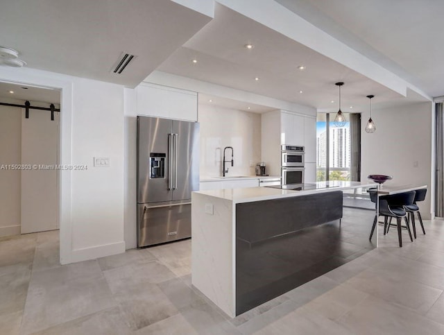 kitchen featuring appliances with stainless steel finishes, a barn door, a center island with sink, and white cabinetry