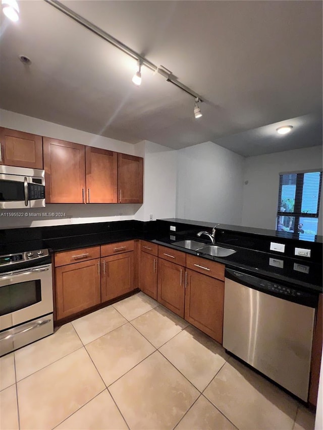 kitchen with rail lighting, sink, dark stone countertops, light tile patterned floors, and stainless steel appliances