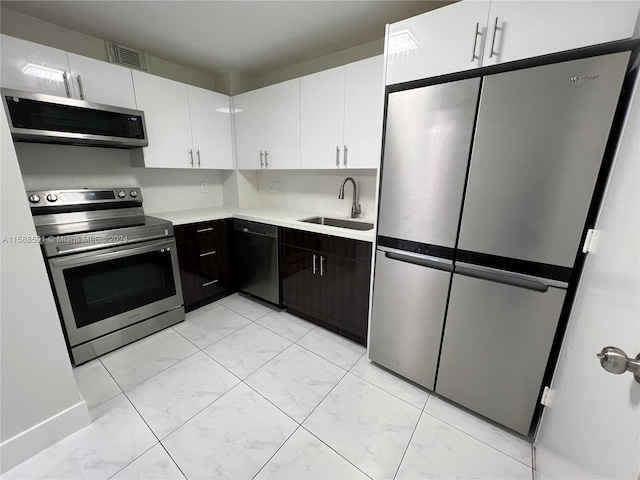 kitchen with stainless steel appliances, dark brown cabinetry, sink, tasteful backsplash, and white cabinetry