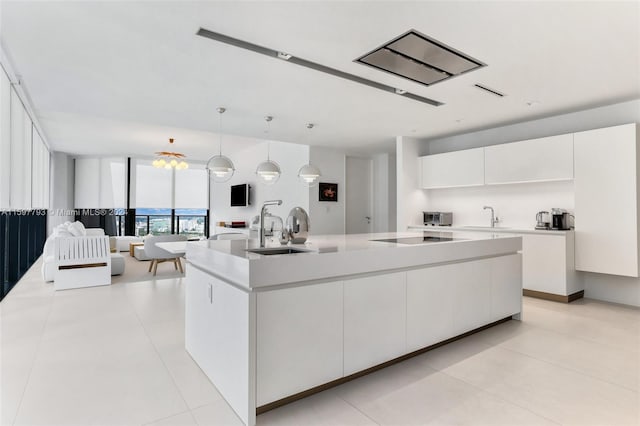 kitchen featuring hanging light fixtures, white cabinets, light tile patterned floors, sink, and a center island with sink