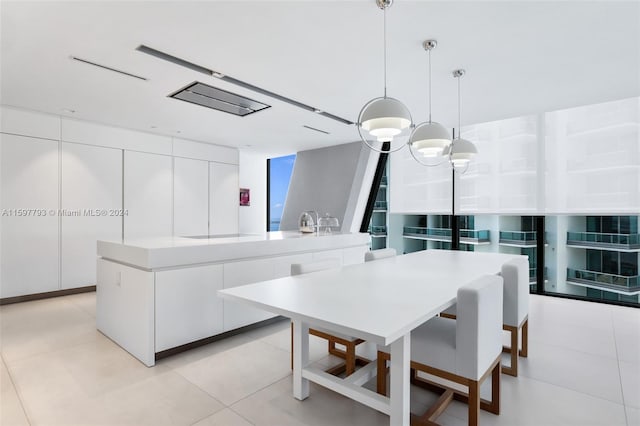 kitchen with an inviting chandelier, pendant lighting, white cabinets, a kitchen island with sink, and light tile patterned floors