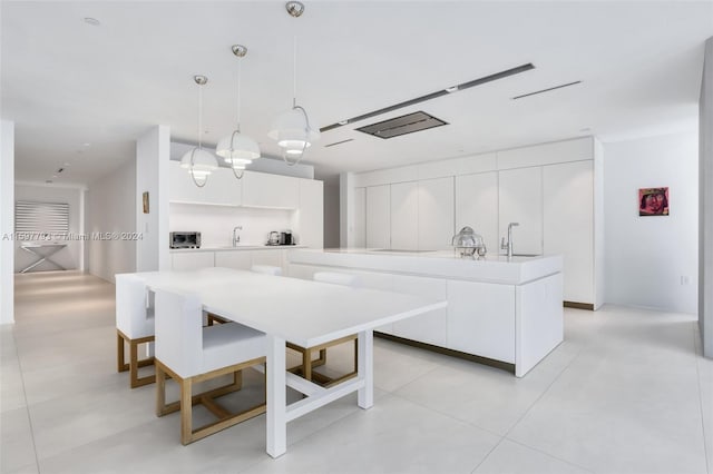 kitchen featuring a kitchen island with sink, white cabinetry, light tile patterned floors, sink, and decorative light fixtures