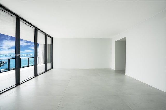 empty room with light tile patterned floors, a wall of windows, and a water view