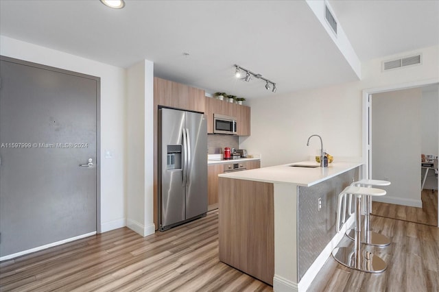 kitchen with a center island with sink, sink, light hardwood / wood-style flooring, appliances with stainless steel finishes, and a breakfast bar area