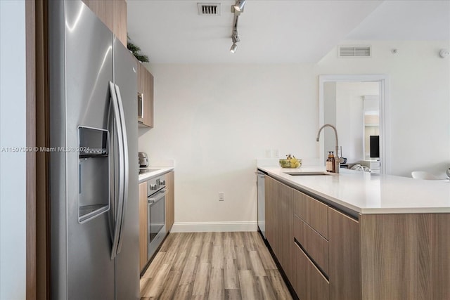 kitchen with kitchen peninsula, appliances with stainless steel finishes, light wood-type flooring, rail lighting, and sink