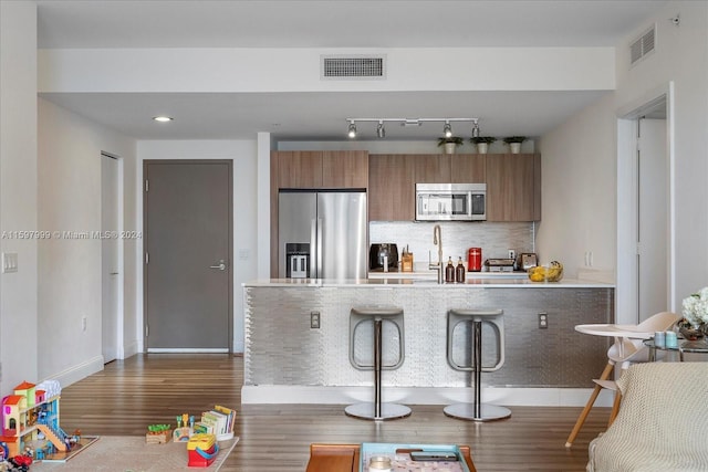 kitchen with kitchen peninsula, appliances with stainless steel finishes, tasteful backsplash, a breakfast bar, and sink