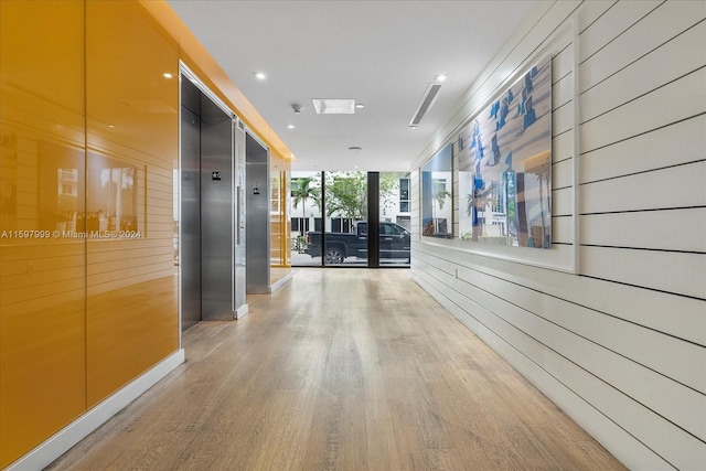 hallway with elevator, hardwood / wood-style flooring, a wall of windows, and wooden walls