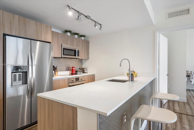 kitchen featuring a breakfast bar, sink, decorative backsplash, appliances with stainless steel finishes, and kitchen peninsula