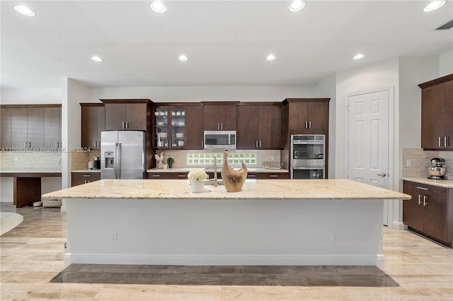 kitchen with a kitchen island with sink, dark brown cabinets, light wood-type flooring, and appliances with stainless steel finishes