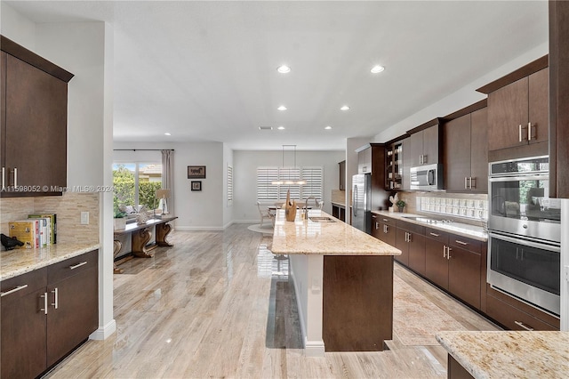 kitchen featuring backsplash, hanging light fixtures, light stone countertops, light hardwood / wood-style floors, and stainless steel appliances