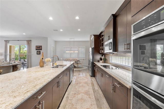 kitchen with appliances with stainless steel finishes, dark brown cabinetry, sink, decorative light fixtures, and light hardwood / wood-style flooring