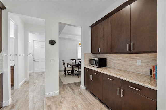 kitchen with backsplash, dark brown cabinetry, light stone countertops, and light hardwood / wood-style floors