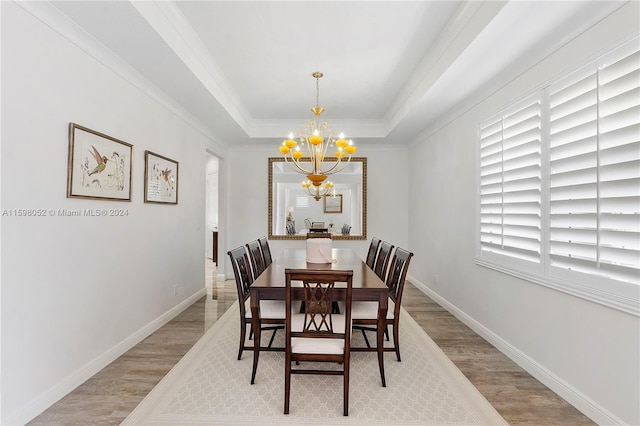 dining room featuring a notable chandelier, plenty of natural light, a raised ceiling, and light wood-type flooring